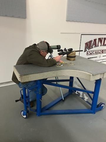 Man shooting a rifle from a bench at a shooting range.