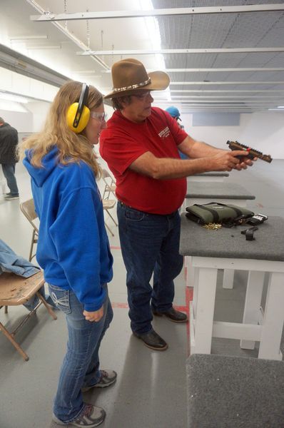 Woman at shooting range with instructor. Instructor in red shirt and cowboy hat shows her how to hold a handgun.