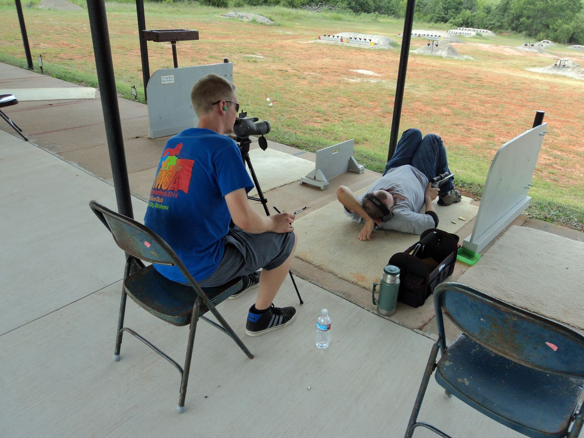 A man sitting in a chair taking a picture of another man laying on the ground