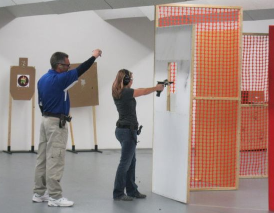 A woman shoots a handgun under supervision at an indoor shooting range.