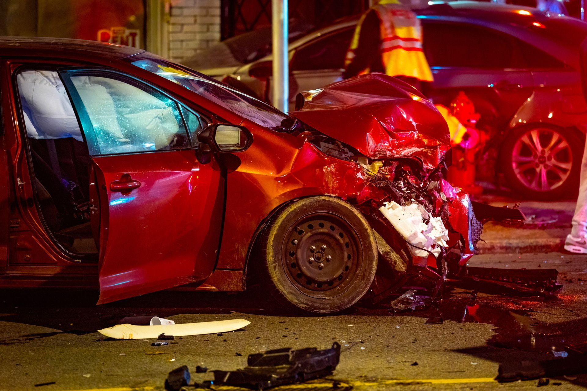 Red car, heavily damaged in a crash, deployed airbags, street scene.
