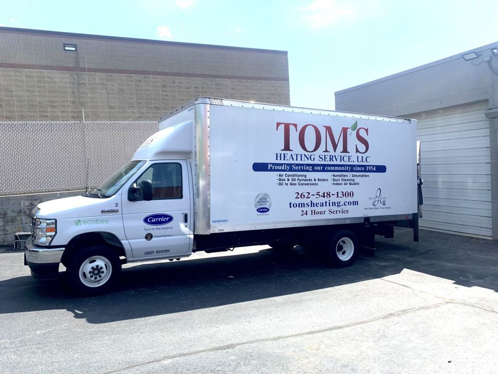 White TOMS delivery truck parked beside a warehouse wall on a sunny day