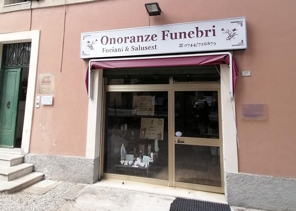 Ingresso di un'impresa di pompe funebri con facciata rosa e porta a vetri, insegna con la scritta 