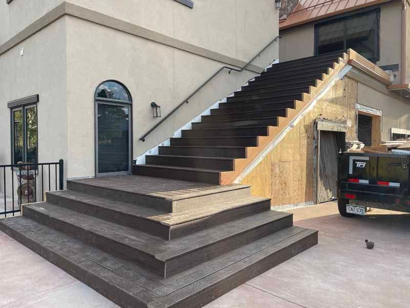 Outdoor wooden staircase with a wide landing leading to a building entrance next to an under-construction wall.