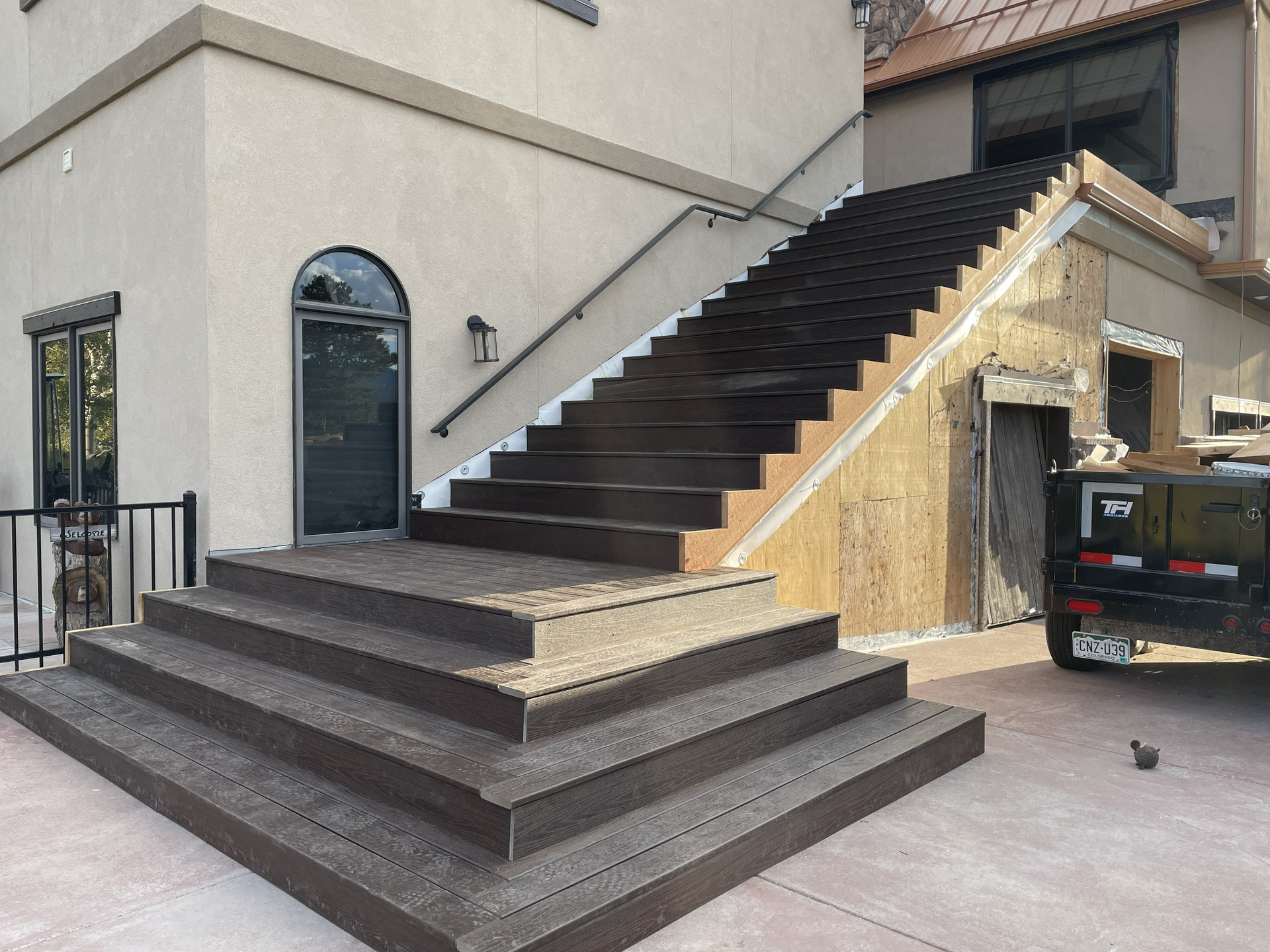 Exterior view of a newly installed dark wood staircase leading up the side of a building under construction.