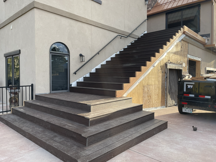 Exterior view of a newly installed dark wood staircase leading up the side of a building under construction.