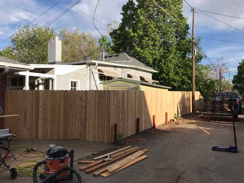 A newly installed wooden privacy fence stands in a residential alleyway with tools and materials scattered nearby.