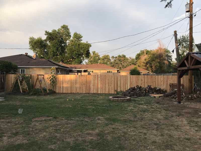 A wooden privacy fence separates a residential backyard from neighboring houses under a cloudy late afternoon sky.