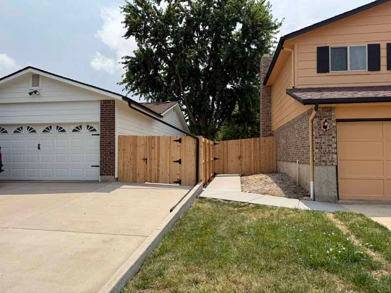 Two houses with a wooden fence and gate separating the side driveway and a concrete walkway.