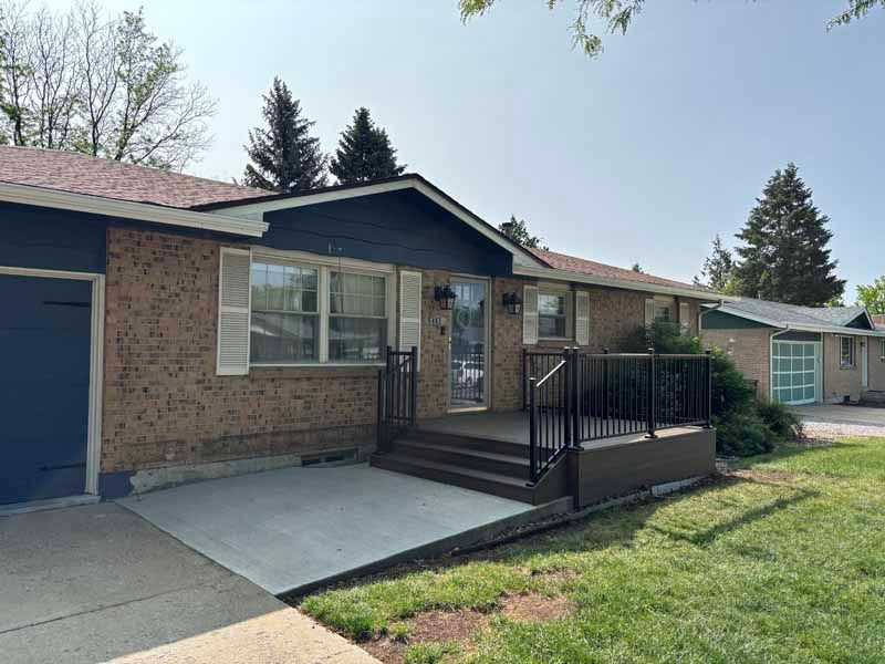 A single-story brick house with a blue front door, a concrete patio, and a newly built wooden deck with black railings.