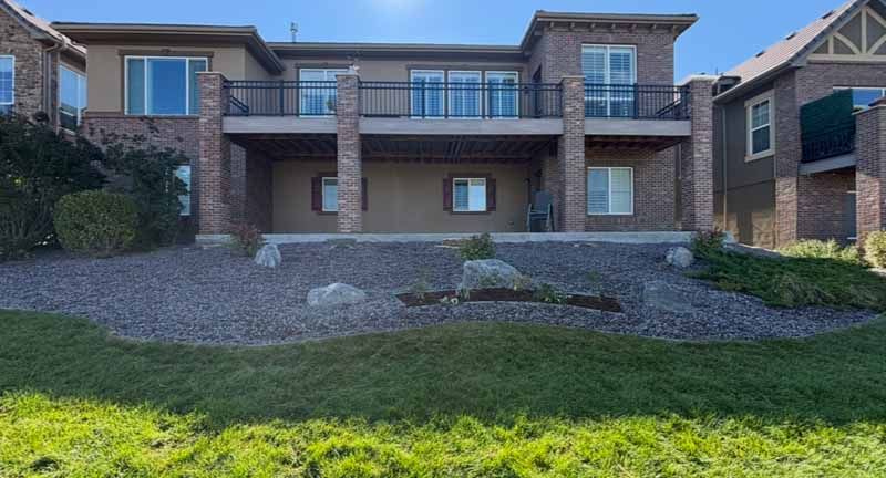 A two-story brick and stucco house with a raised rear deck, patio, and a landscaped gravel yard in a sunny residential area.