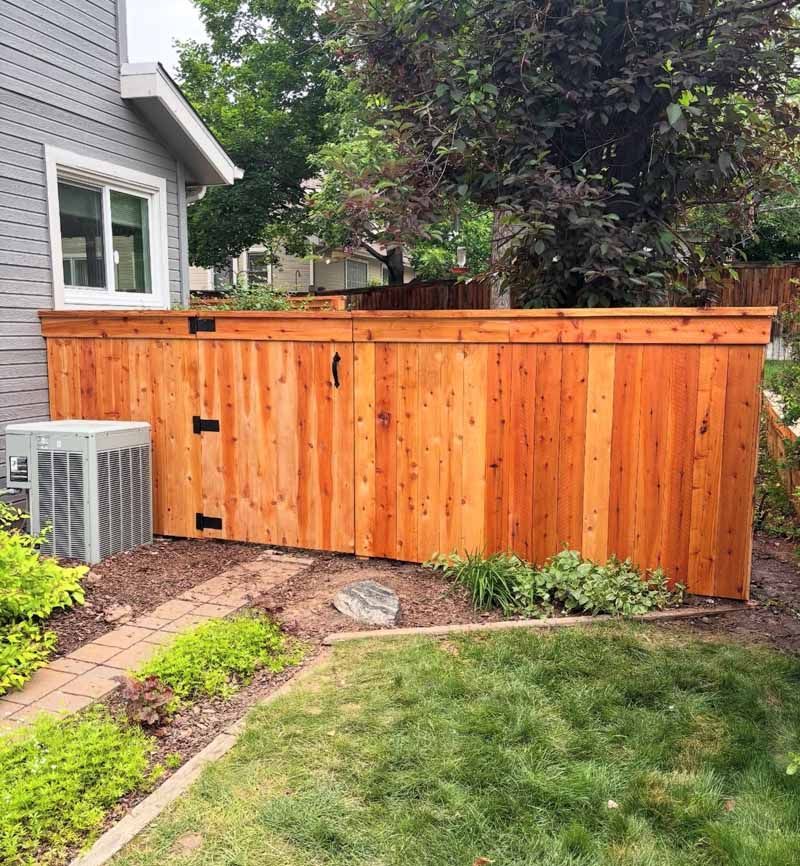 A stained cedar privacy fence installed next to a gray house with an outdoor air conditioning unit in the foreground.