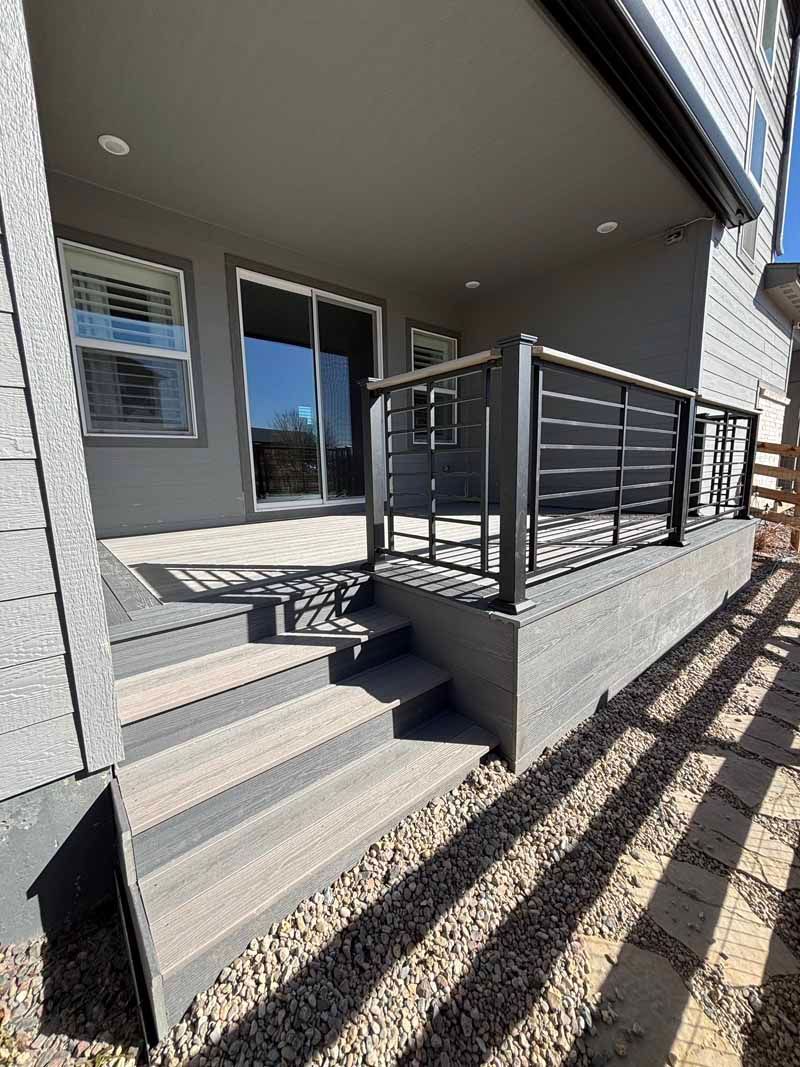 A low-angle view of a grey composite deck with stairs, a metal railing, and a sliding glass door leading into a home.