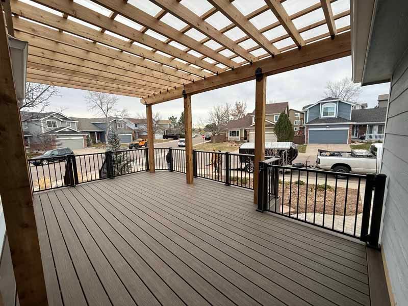 A wooden pergola covers a composite deck with black metal railings, overlooking a suburban street.