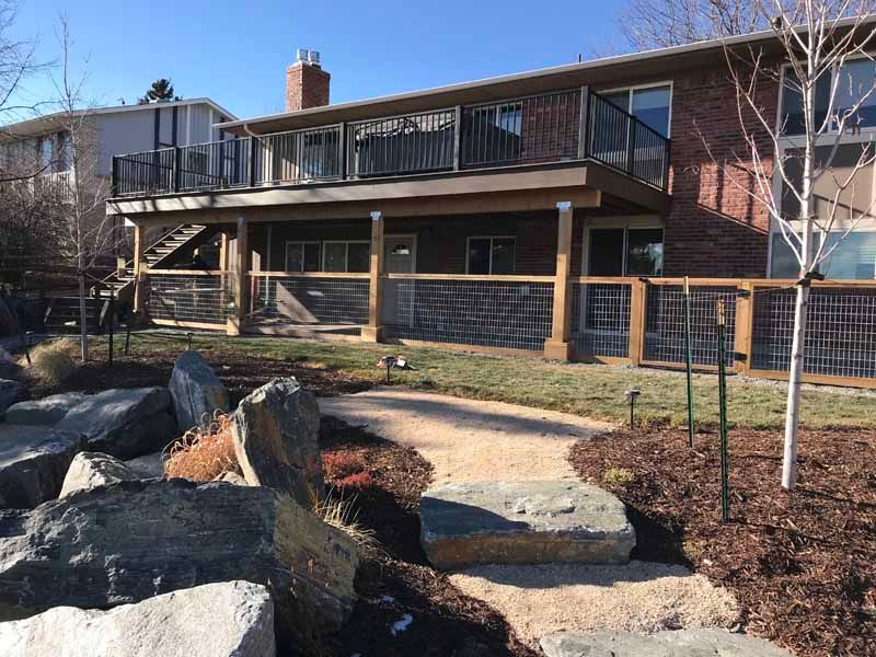 A backyard with a gravel path, large rocks, and a raised wooden deck attached to a brick house.