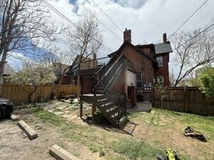 A brick house exterior with a metal staircase leading to an elevated deck in a residential backyard.