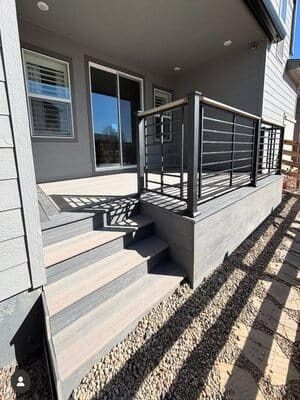 A gray-toned composite deck and staircase featuring a black metal horizontal railing, set against a modern house exterior.