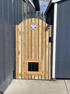 A wooden gate with vertical slats and black metal spikes at the top, positioned between two blue exterior walls.