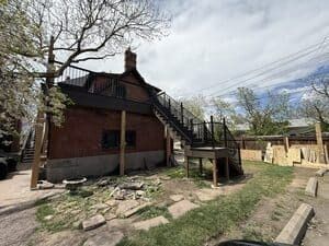 A brick two-story building features an exterior black metal staircase leading to a second-floor deck in a grassy yard.