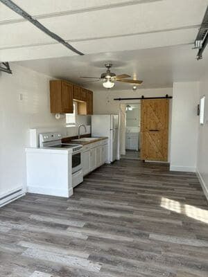 A small kitchen area with white cabinets, wood upper cabinets, wood-look flooring, and a rustic barn door in the back.