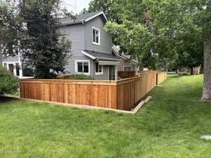 A grey house with a new, horizontal wood fence in the backyard surrounded by a green lawn and mature trees.