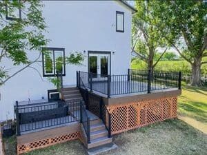 A two-level composite deck with black railings and wood-patterned lattice skirting attached to a white house exterior.