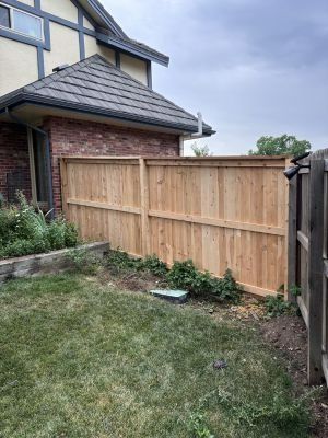 A new light-colored wood privacy fence stands in a grassy backyard next to a brick and stucco house.