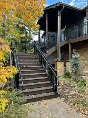 Dark wooden staircase with black railings leading up to a brown house exterior surrounded by autumn leaves.