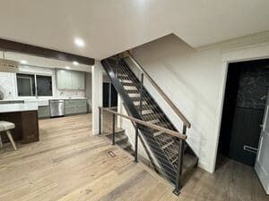 A modern interior with light wood flooring, an open kitchen, and a staircase with metal railings leading to an upper level.
