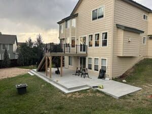 A light yellow house with a raised wooden deck leading down to a new, unfinished concrete patio in the backyard.