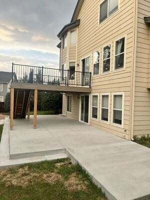 A tan two-story house with a newly poured concrete patio and an elevated deck with black railings.