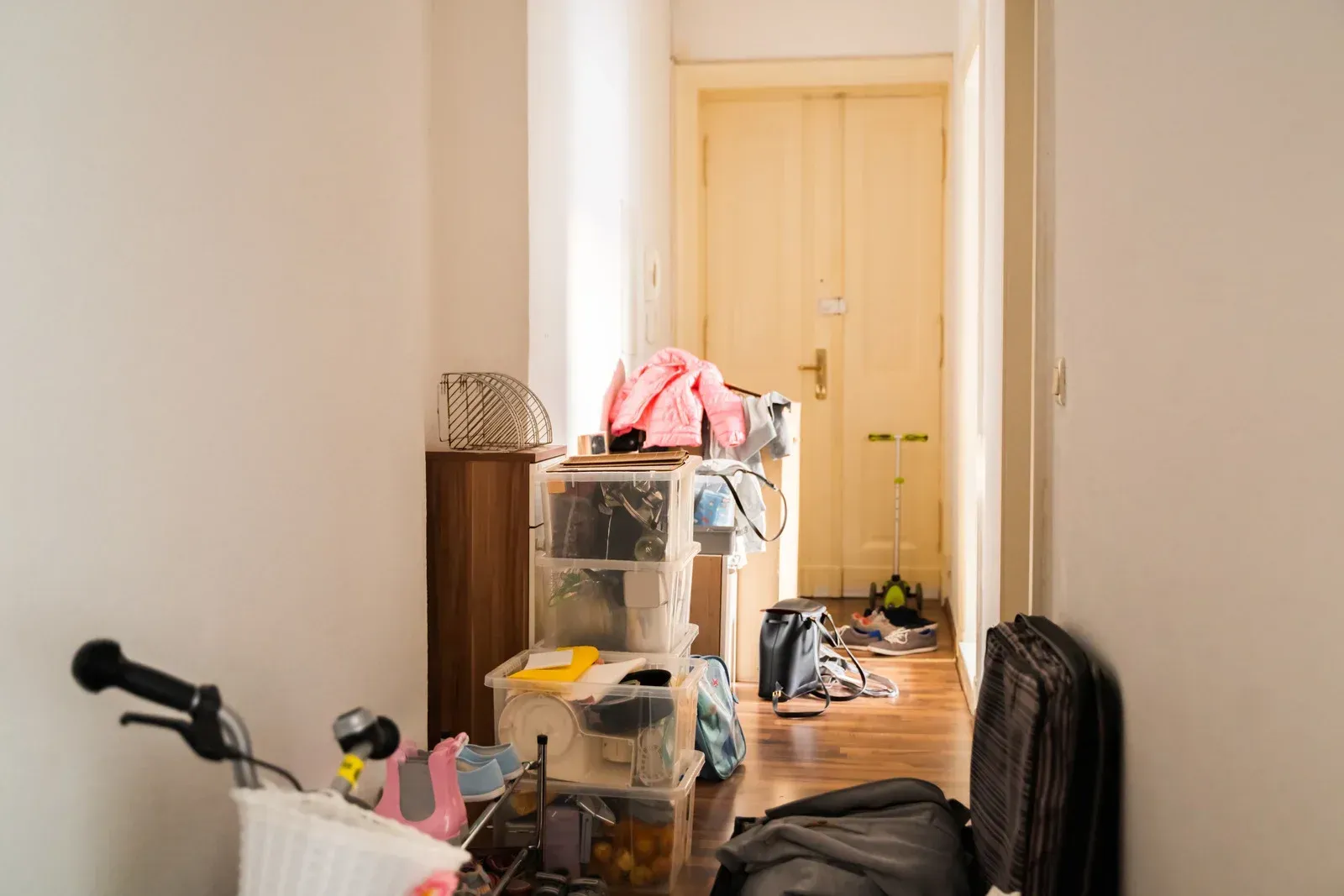 Cluttered hallway with boxes, clothes, and a stroller leading to a closed yellow door