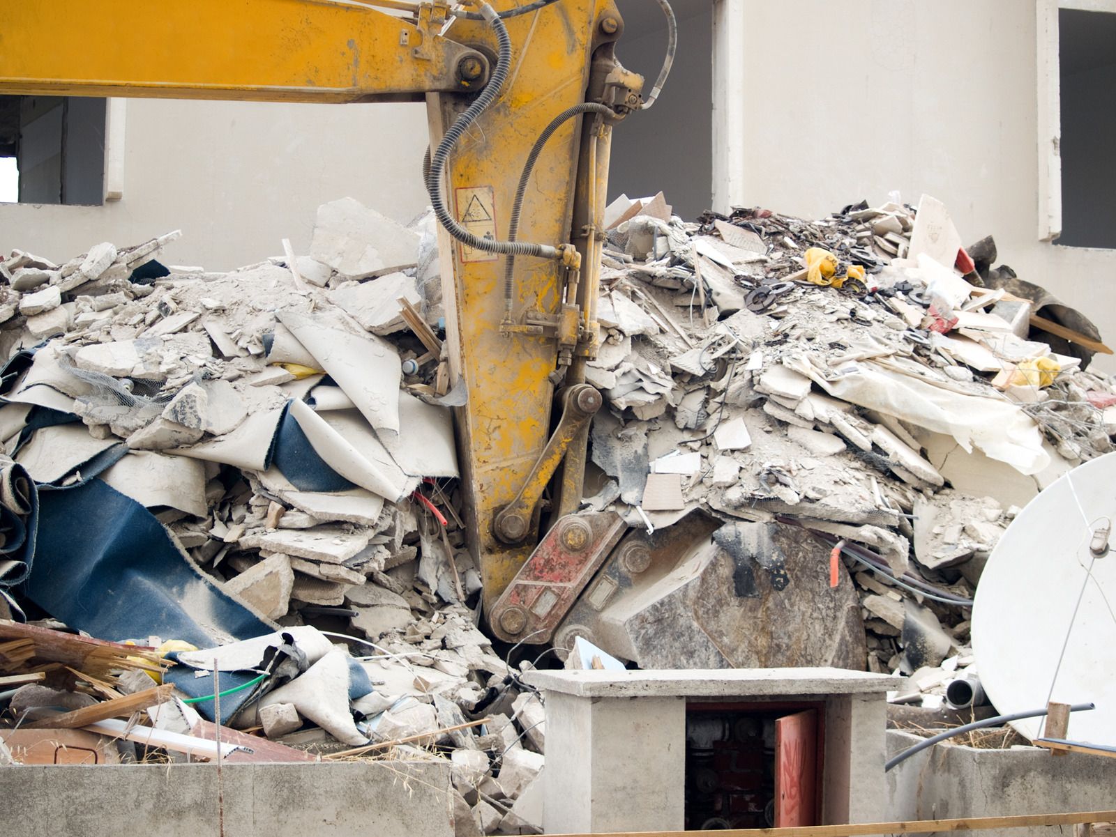 Excavator arm amid rubble at a demolition site with broken concrete and debris pile