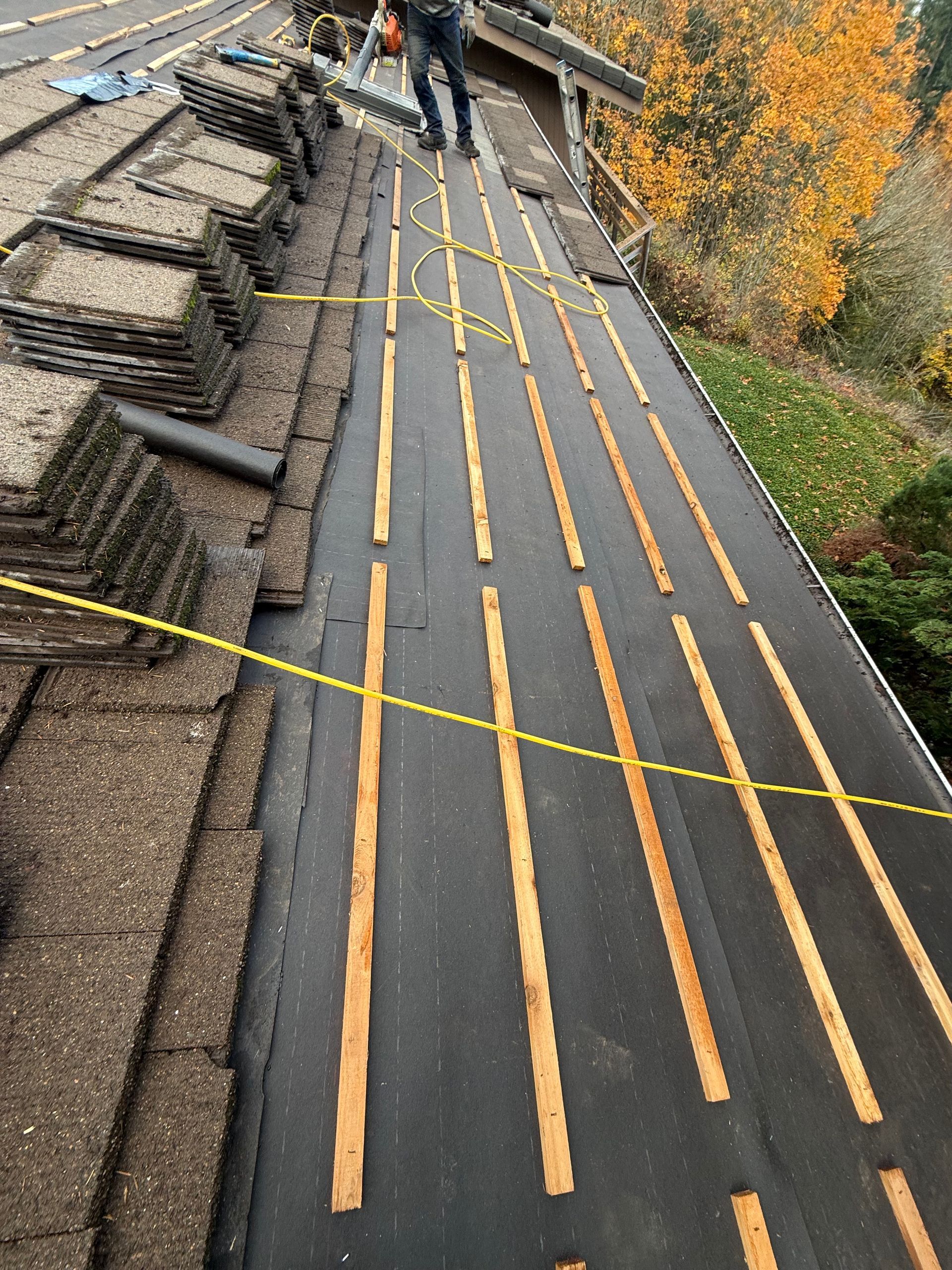 House roof partially re-roofed; some black tiles, some exposed wood. A red lift crane is present. Outdoors, sunny.