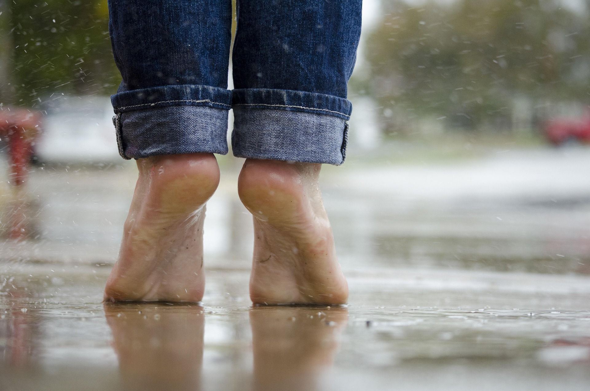 Blote voeten in opgerolde spijkerbroekspijpen op een natte stoep in de regen.