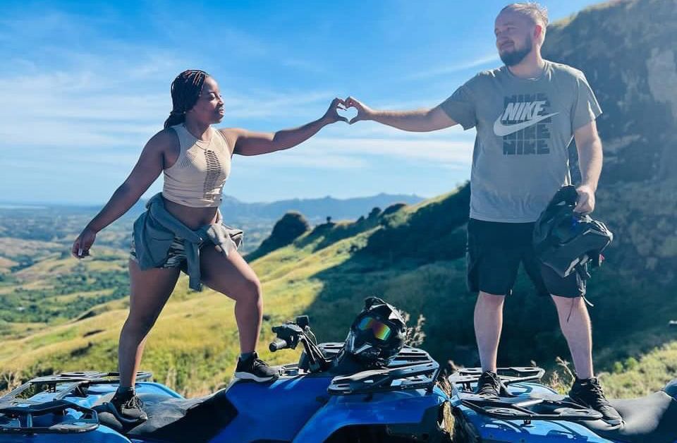 A man and a woman are making a heart shape with their hands while standing on top of an atv.
