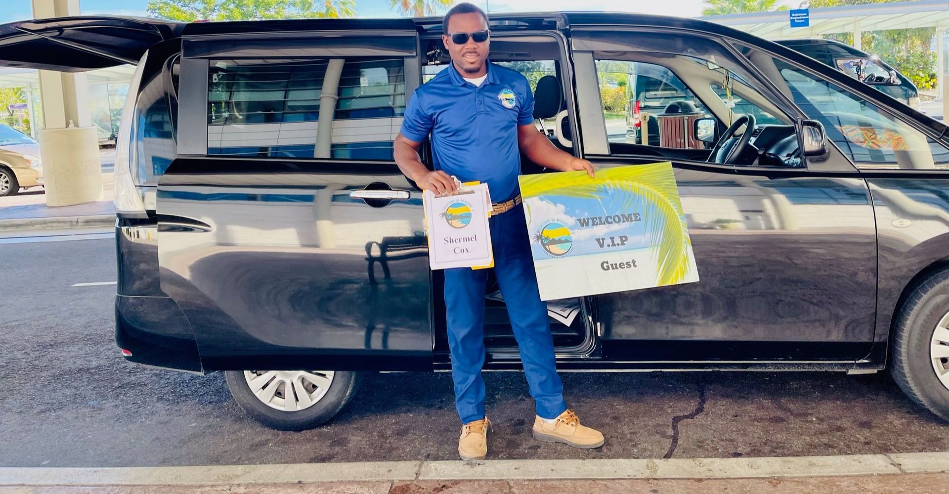 A man is standing in front of a black van holding two bags.