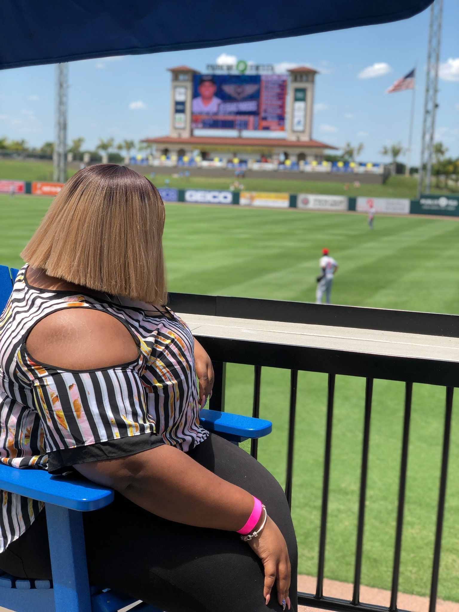 A woman is sitting in a blue chair watching a baseball game
