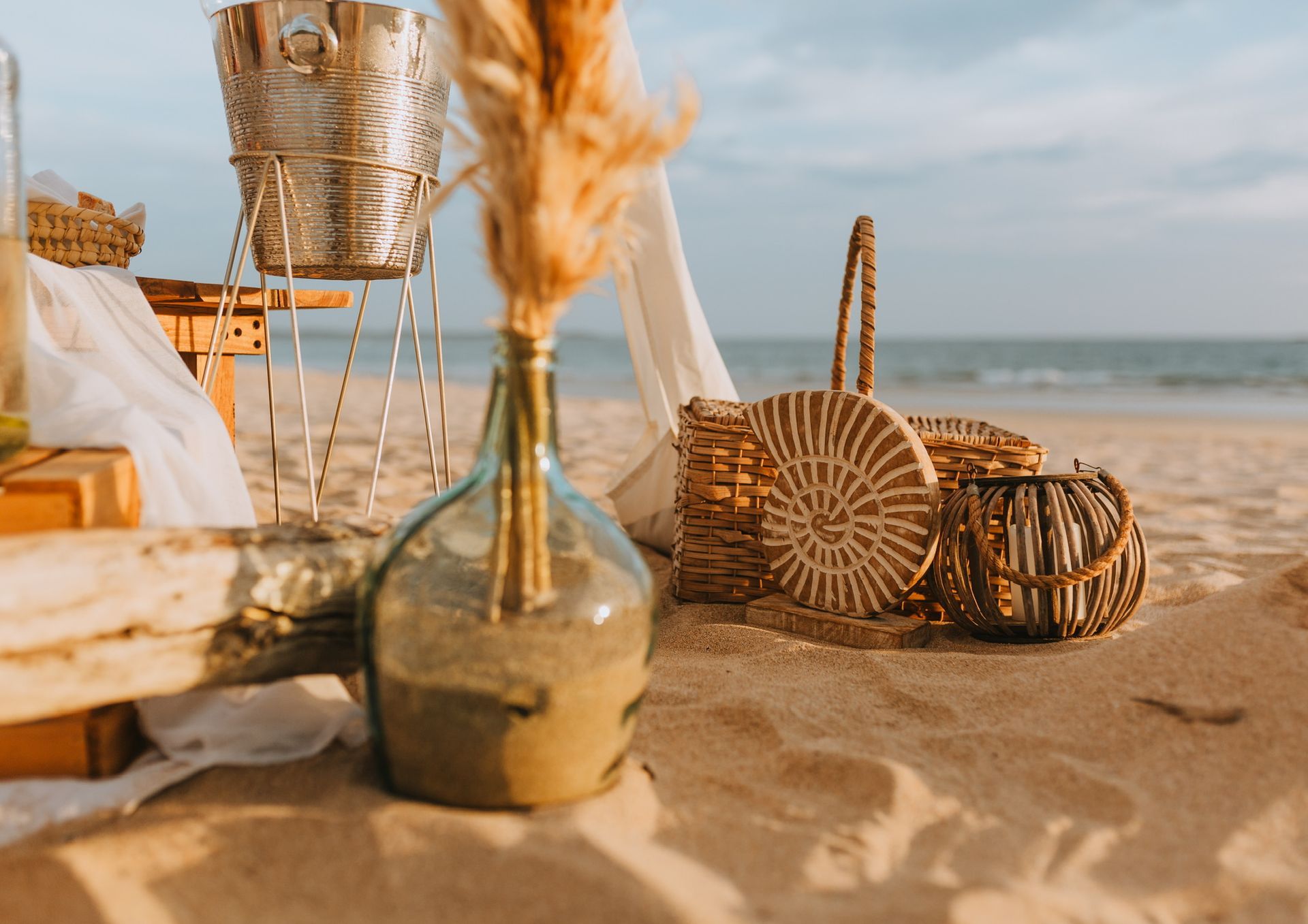 A vase of flowers is sitting on the beach next to a wicker basket.