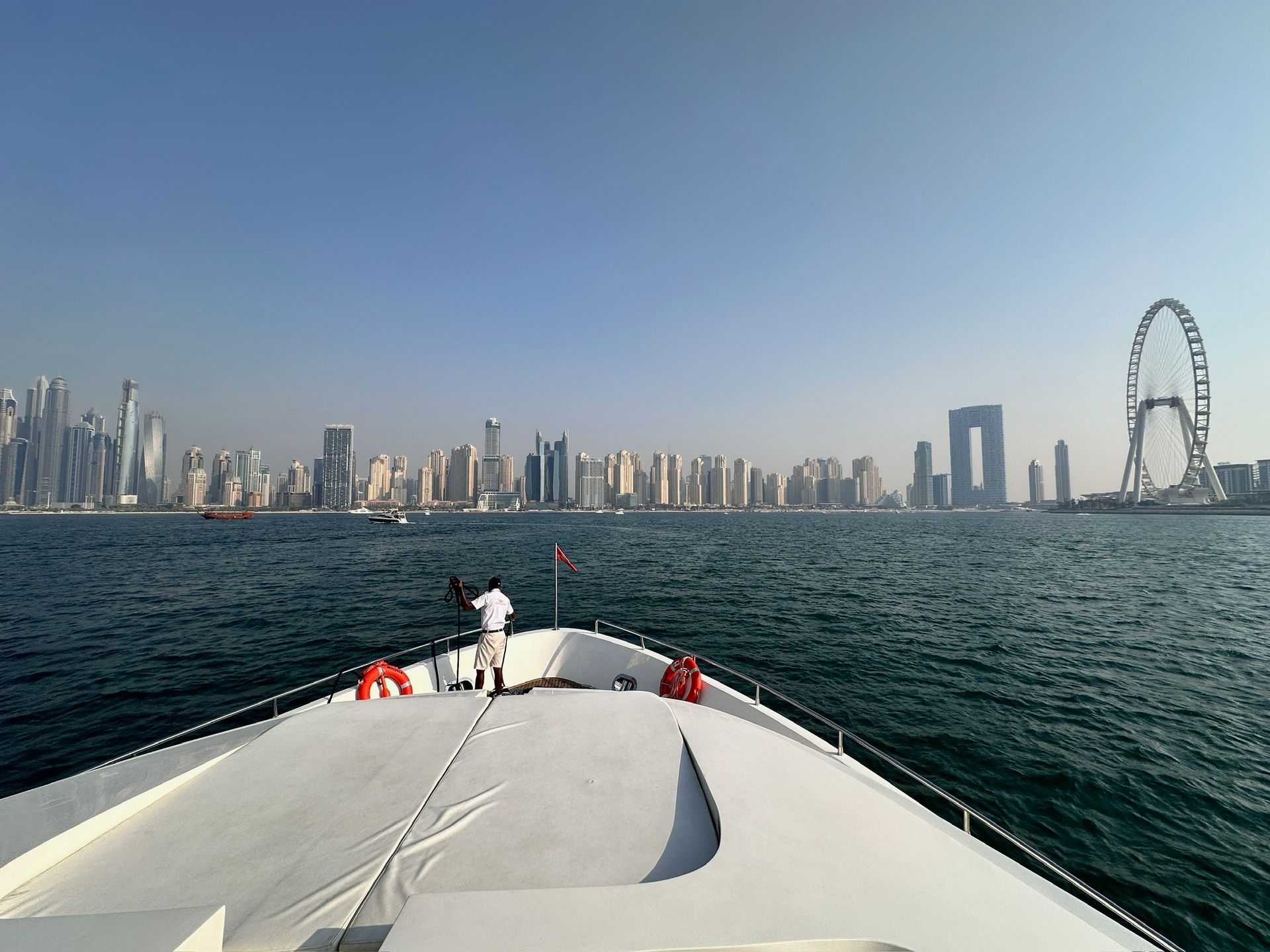 A man is standing on the bow of a boat looking at the city skyline.