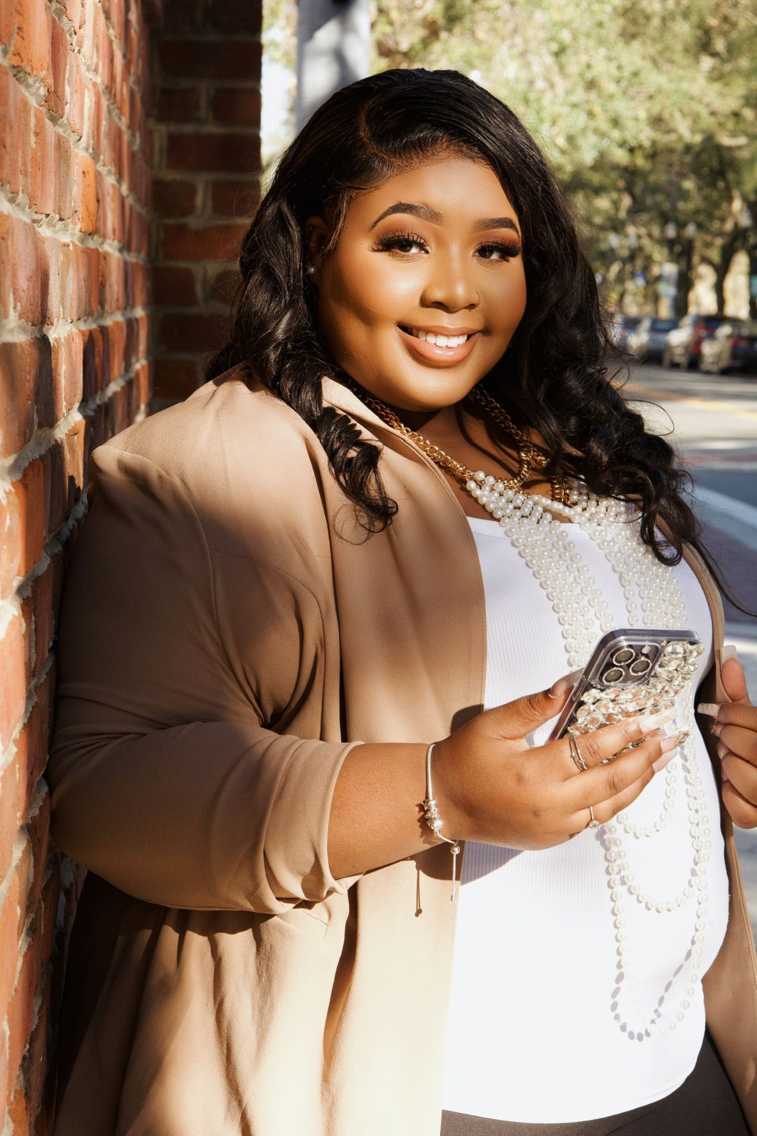 A plus size woman is leaning against a brick wall while holding a cell phone.