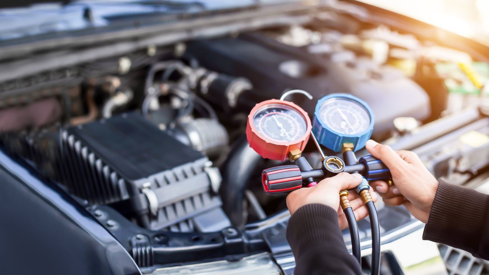 Person using gauges to check a car's air conditioning system in an engine bay.