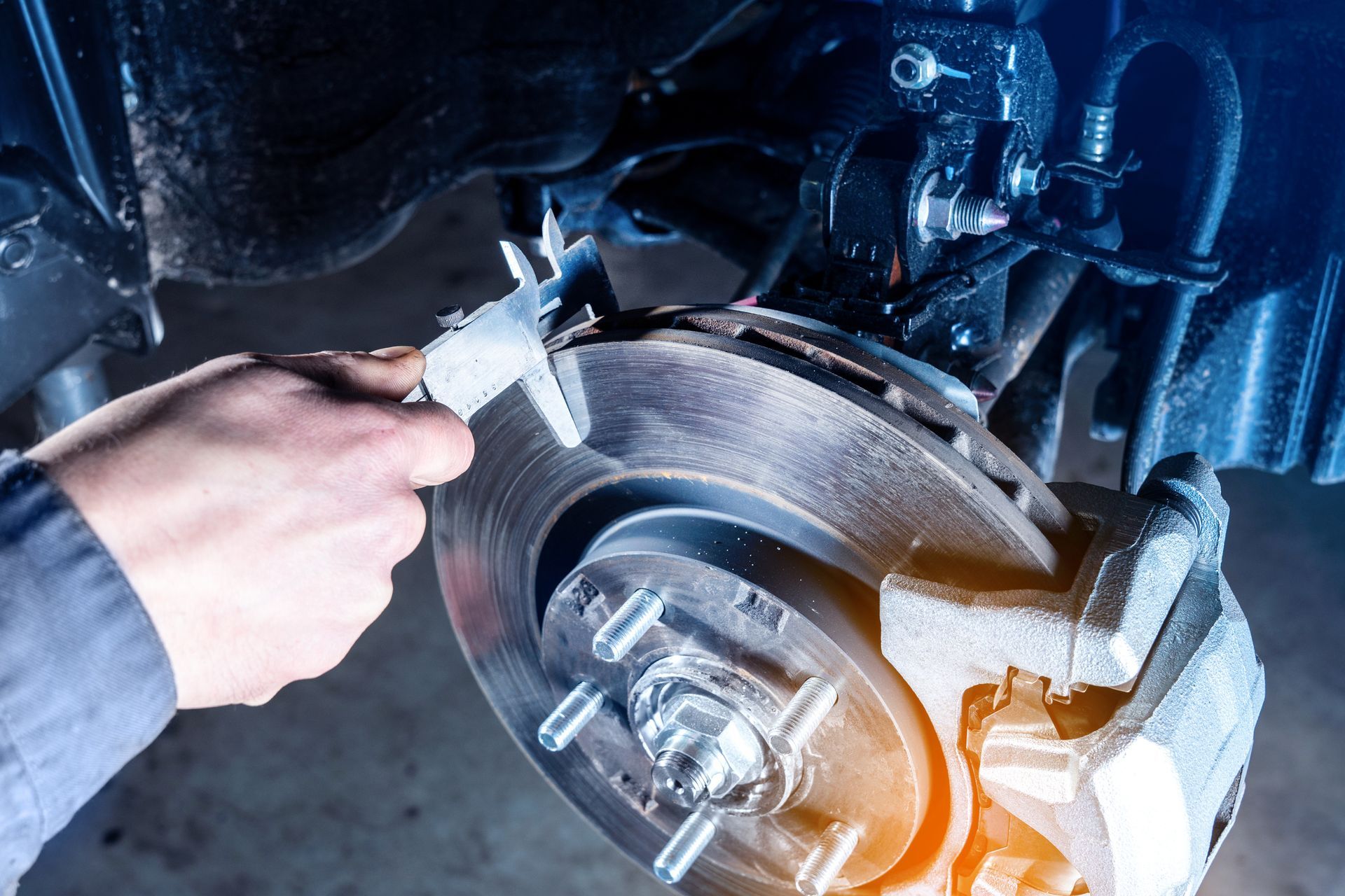 Mechanic measuring a car's brake rotor with calipers. Close-up view in a repair shop.