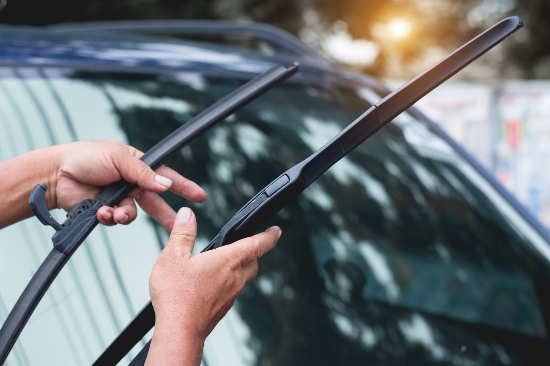 Hands replacing a windshield wiper on a blue car.