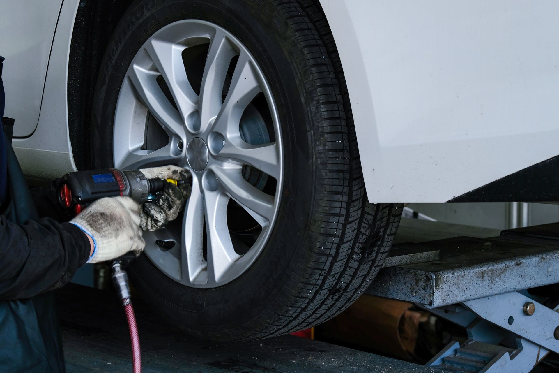 Mechanic using an impact wrench to remove a car's wheel, on a lift.