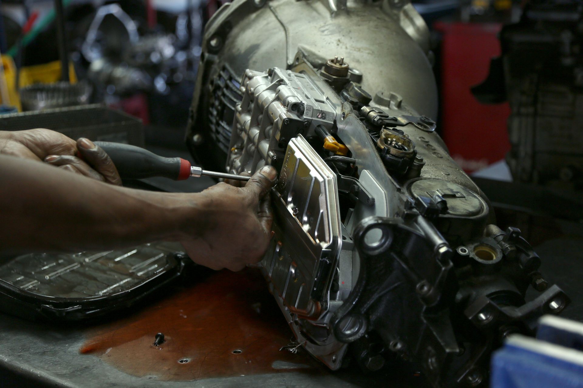 Mechanic using a screwdriver to remove a panel on a car transmission in a repair shop.