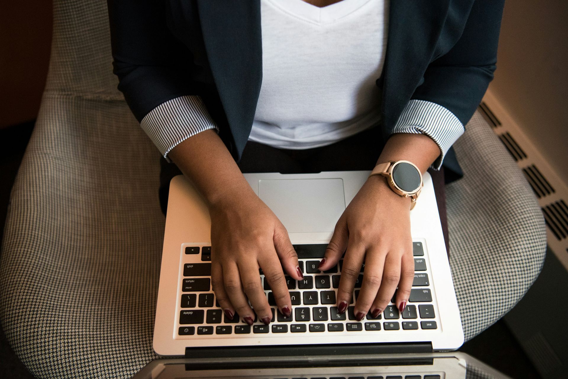 Person typing on a laptop while seated, wearing a black cardigan and white top, with a wristwatch visible.