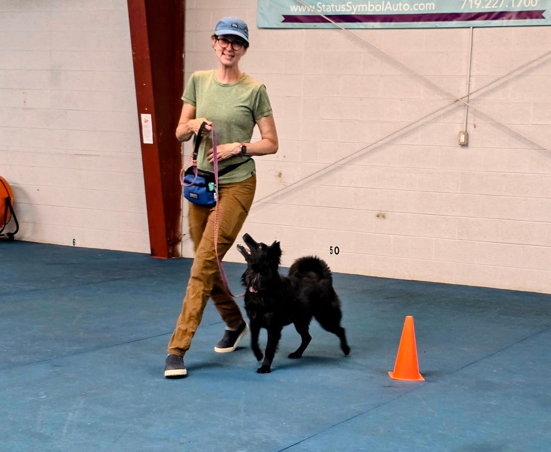 A heeler mix and her baseball hat clad mom practice Rally Obedience.