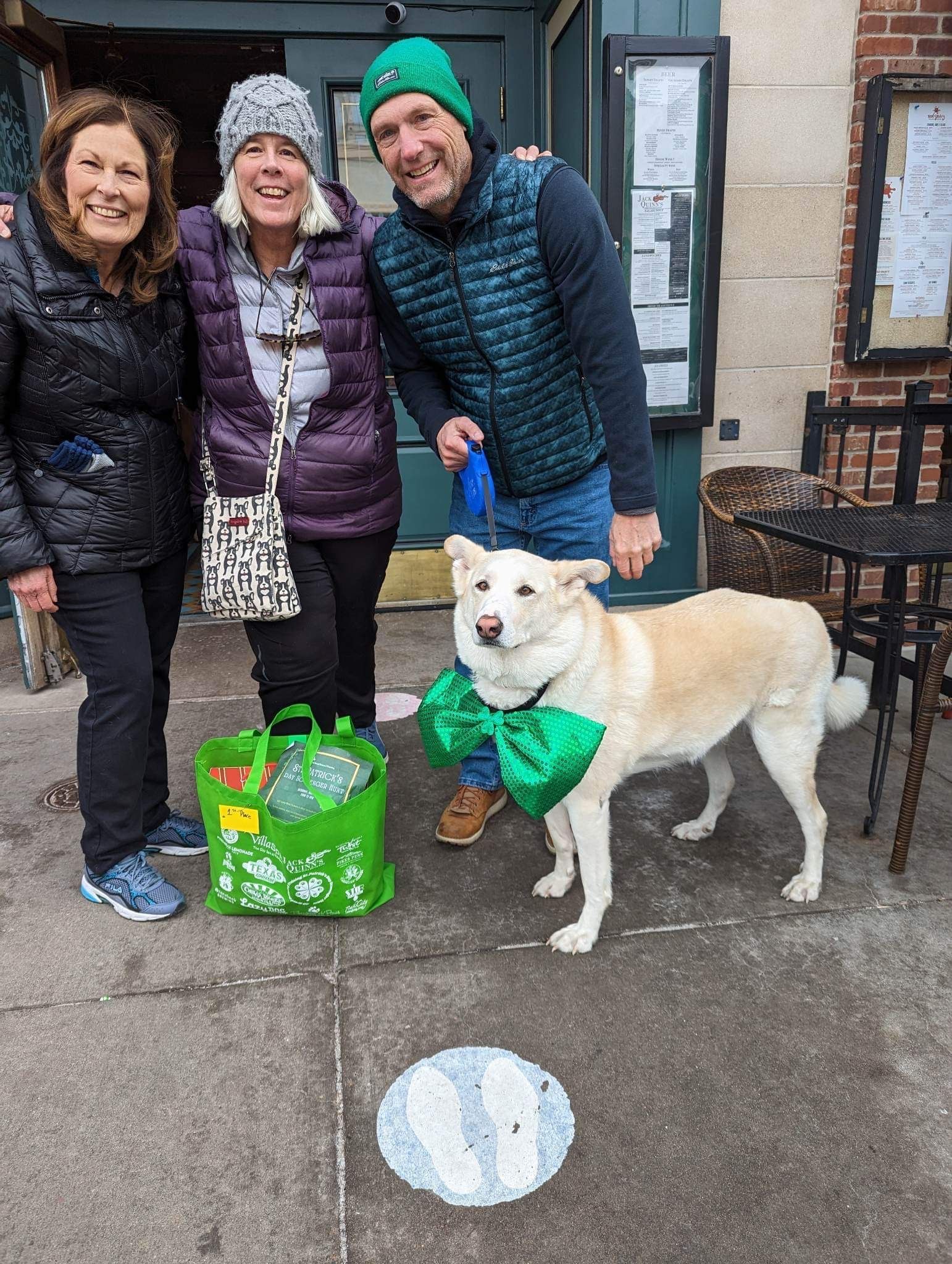 Three people posing with their dog in front of a pub.
