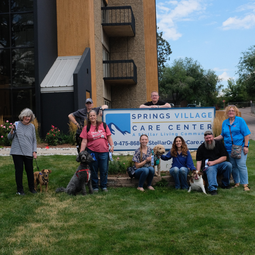 A graduating Therapy Dog class poses in front of a sign.